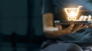hand holding laptop with graphic of shopping cart on top