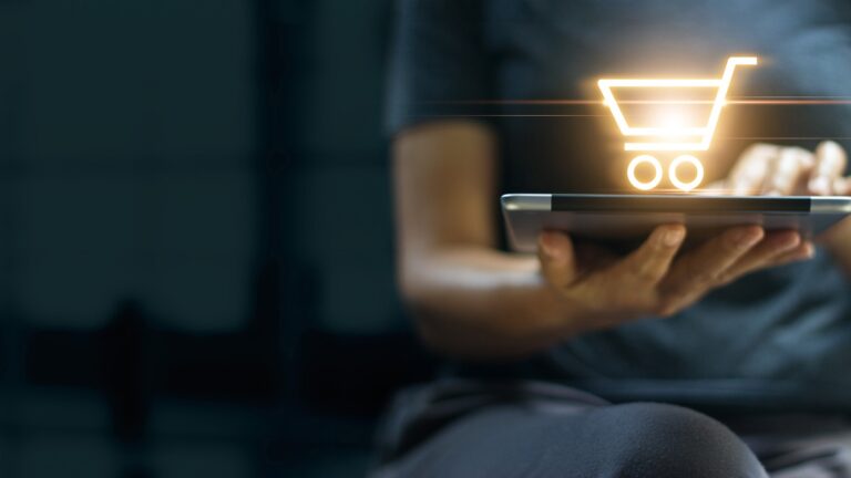 hand holding laptop with graphic of shopping cart on top
