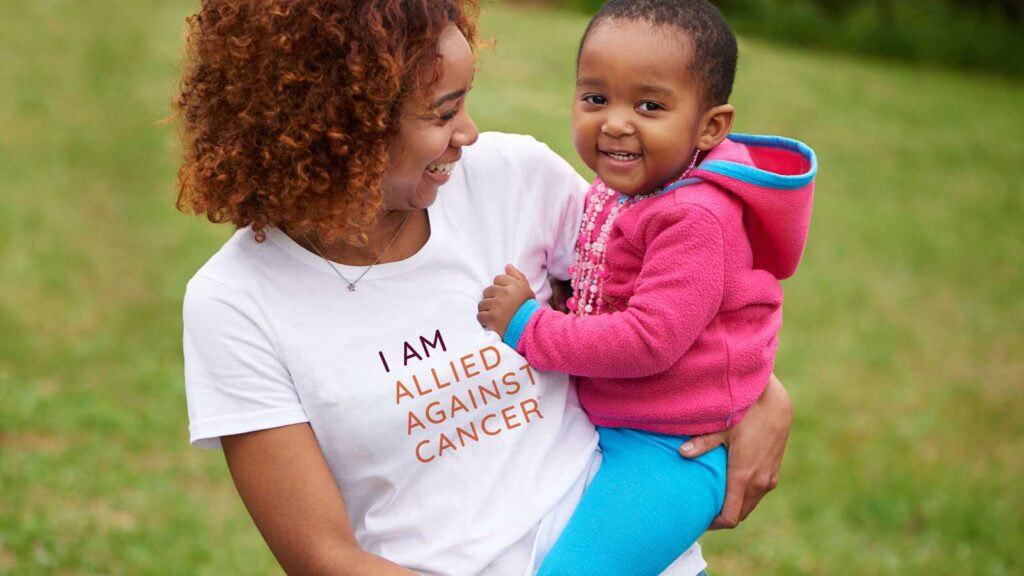 black woman wearing allied against cancer shirt holding a black child