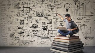 man sitting on stack of books with wall full of equations