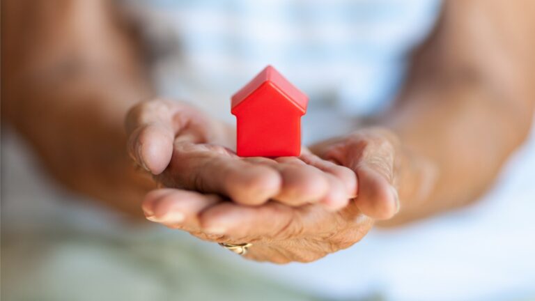 Photo of an elderly woman holding a small red house