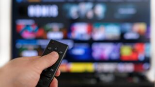 Photo of a hand holding a remote control up to an internet-connected television