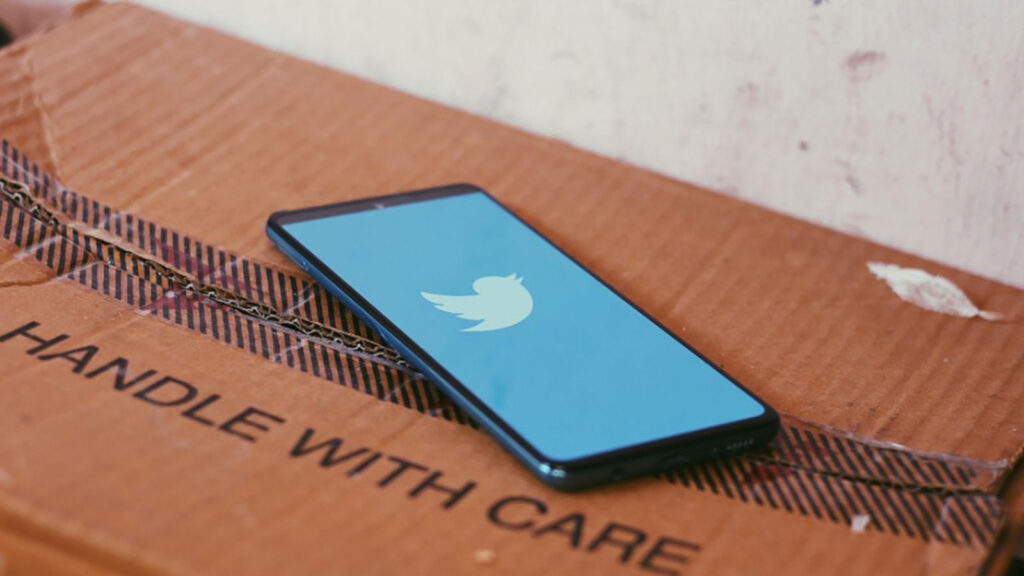 Phone displaying Twitter atop of a box that reads Handle With Care
