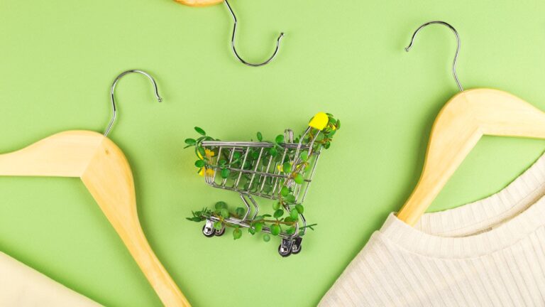 Shopping cart entwined with plants on green background among hangers. Sustainable eco lifestyle.